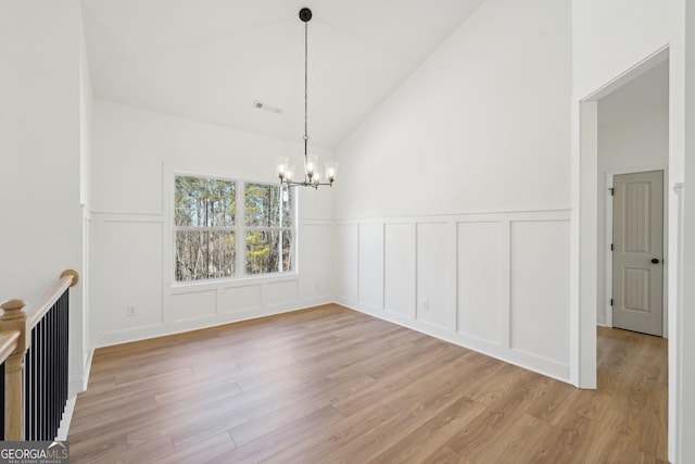 unfurnished dining area featuring high vaulted ceiling, a chandelier, and light wood-type flooring