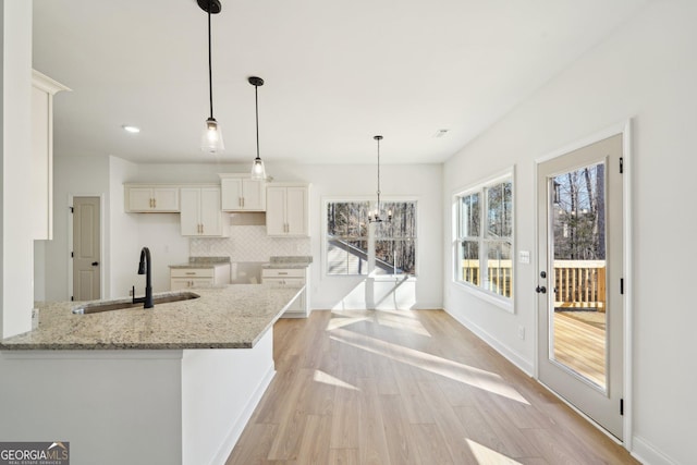 kitchen featuring white cabinetry, sink, decorative backsplash, hanging light fixtures, and light stone countertops