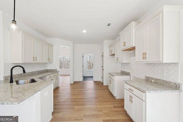 kitchen with white cabinetry, light stone countertops, sink, and hanging light fixtures