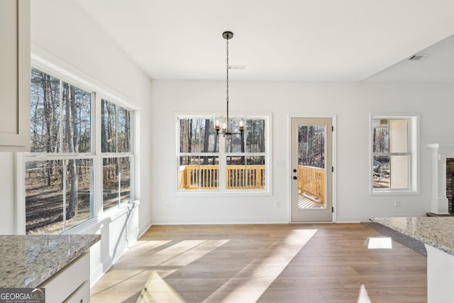 unfurnished dining area featuring an inviting chandelier, plenty of natural light, and light hardwood / wood-style flooring