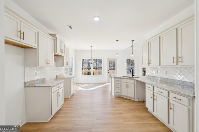 kitchen featuring pendant lighting, sink, tasteful backsplash, kitchen peninsula, and light wood-type flooring