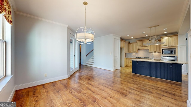 kitchen with pendant lighting, a center island with sink, crown molding, decorative backsplash, and appliances with stainless steel finishes