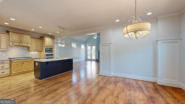 kitchen with decorative backsplash, light brown cabinets, ceiling fan with notable chandelier, and a center island with sink