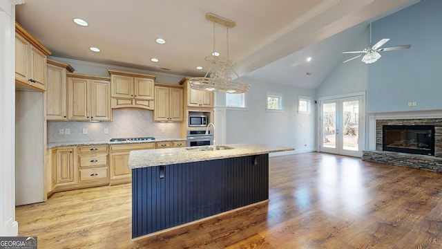 kitchen featuring light stone countertops, backsplash, stainless steel appliances, a kitchen island with sink, and light brown cabinets