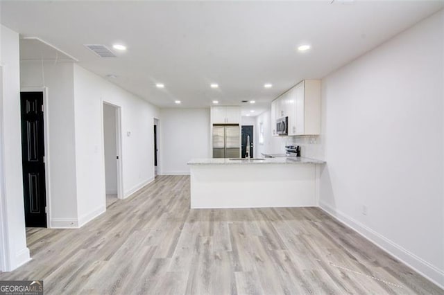 kitchen with kitchen peninsula, appliances with stainless steel finishes, light stone countertops, light hardwood / wood-style floors, and white cabinetry