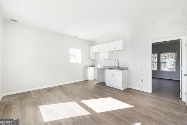 kitchen featuring light stone countertops, sink, wood-type flooring, and white cabinets