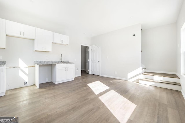 kitchen with light wood-type flooring, white cabinets, and light stone counters