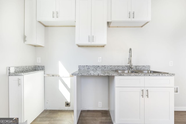 kitchen featuring light stone countertops, sink, white cabinets, and hardwood / wood-style flooring