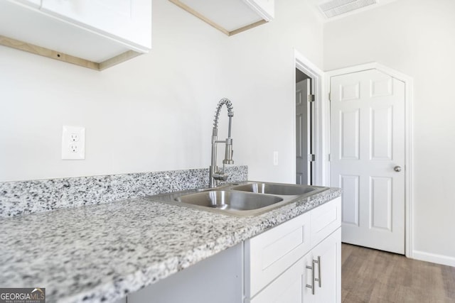 kitchen featuring light stone counters, sink, wood-type flooring, and white cabinets