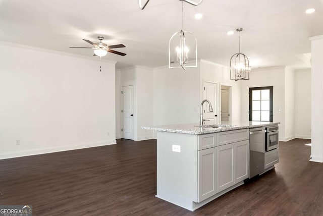 kitchen with a center island with sink, pendant lighting, sink, and dark wood-type flooring