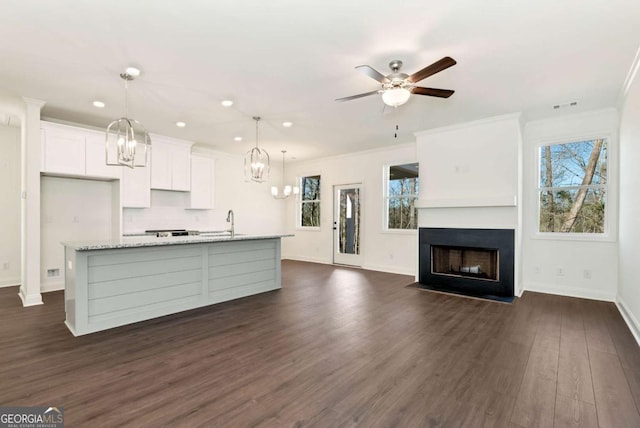 kitchen with a center island with sink, ceiling fan, decorative light fixtures, light stone counters, and white cabinetry