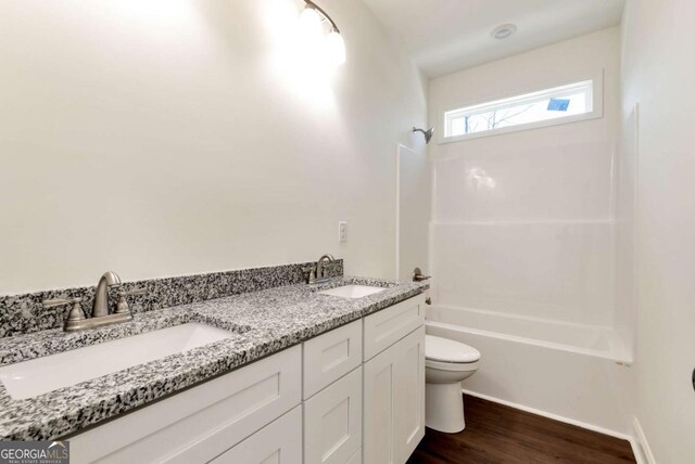 full bathroom with hardwood / wood-style flooring, vanity, tub / shower combination, and toilet