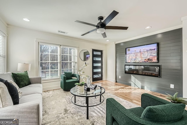 living room with ceiling fan, hardwood / wood-style floors, crown molding, and wood walls