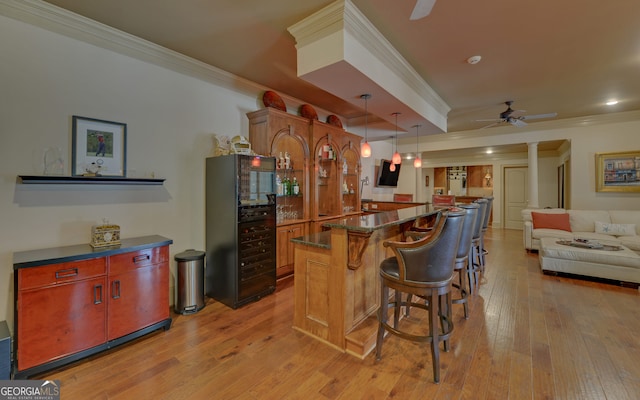 kitchen with ceiling fan, a kitchen breakfast bar, crown molding, decorative light fixtures, and light wood-type flooring