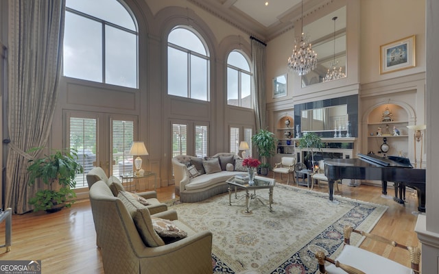 living room with light hardwood / wood-style floors, built in shelves, a healthy amount of sunlight, and a towering ceiling