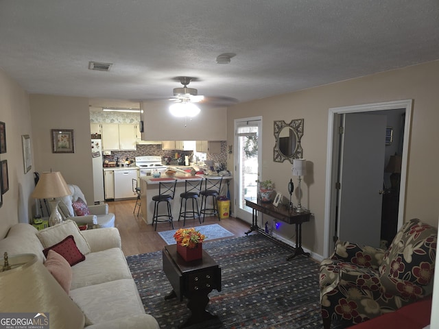 living room featuring ceiling fan, light hardwood / wood-style flooring, and a textured ceiling