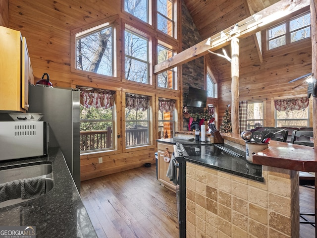 kitchen with dark hardwood / wood-style floors, wood walls, a kitchen bar, and high vaulted ceiling