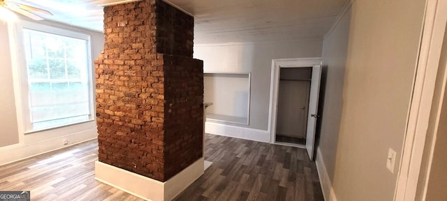 hallway with baseboards, wood finished floors, and brick wall