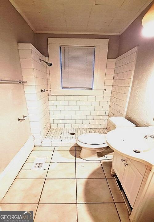 bathroom featuring tile patterned flooring, toilet, vanity, and a tile shower