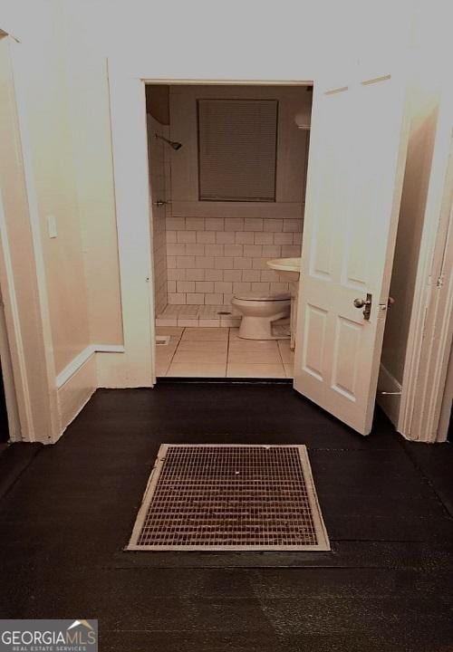 bathroom featuring toilet, a shower, and wood finished floors