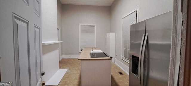 kitchen with a center island, baseboards, stainless steel fridge, and a sink