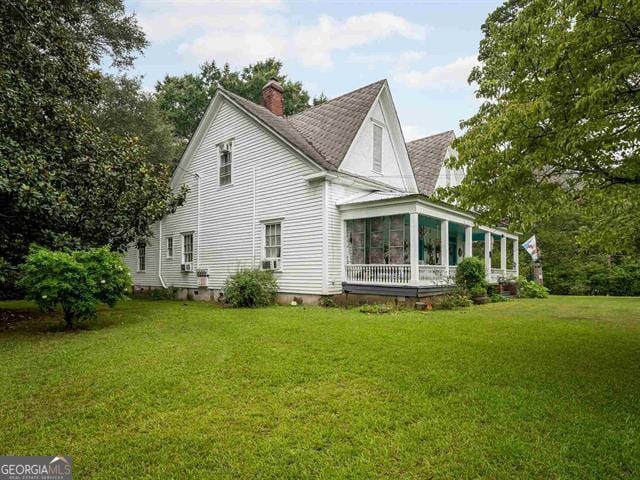 back of property with a shingled roof, a chimney, a yard, and a sunroom