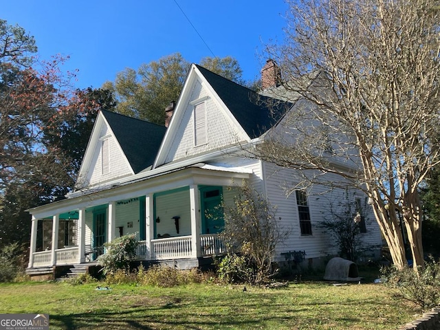 view of side of property featuring a porch, a chimney, and a yard