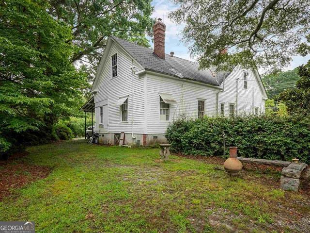 back of house with crawl space, a chimney, and a yard