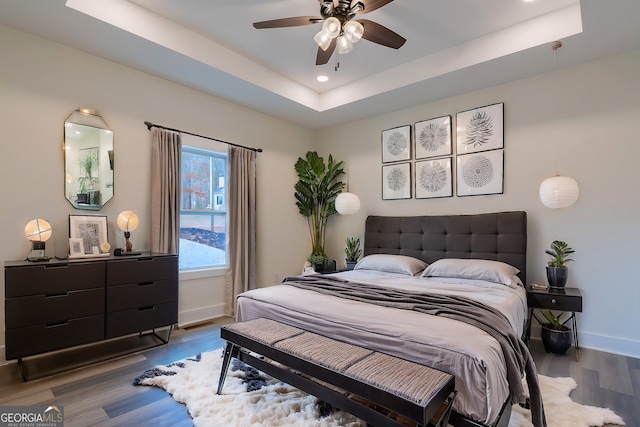 bedroom featuring recessed lighting, a raised ceiling, baseboards, and wood finished floors