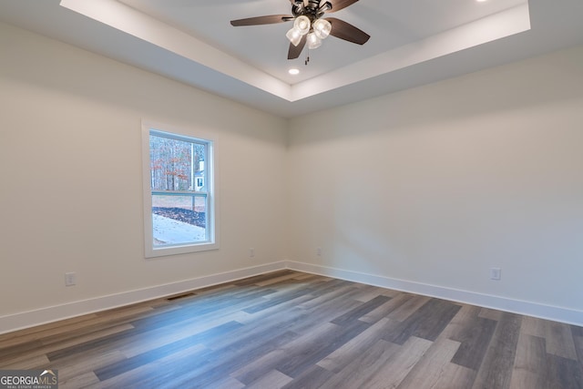 spare room with a ceiling fan, visible vents, baseboards, dark wood-style flooring, and a raised ceiling