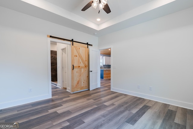 unfurnished room featuring a barn door, baseboards, a ceiling fan, and wood finished floors