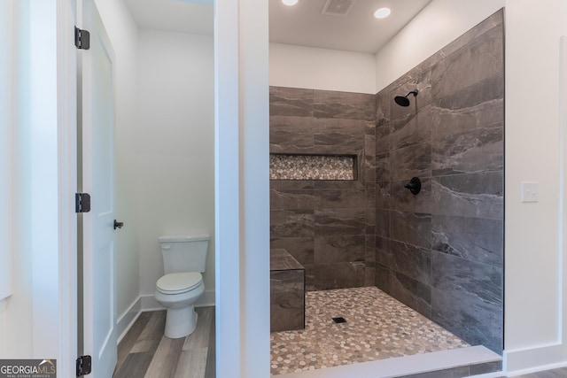 full bathroom with visible vents, toilet, wood finished floors, baseboards, and tiled shower