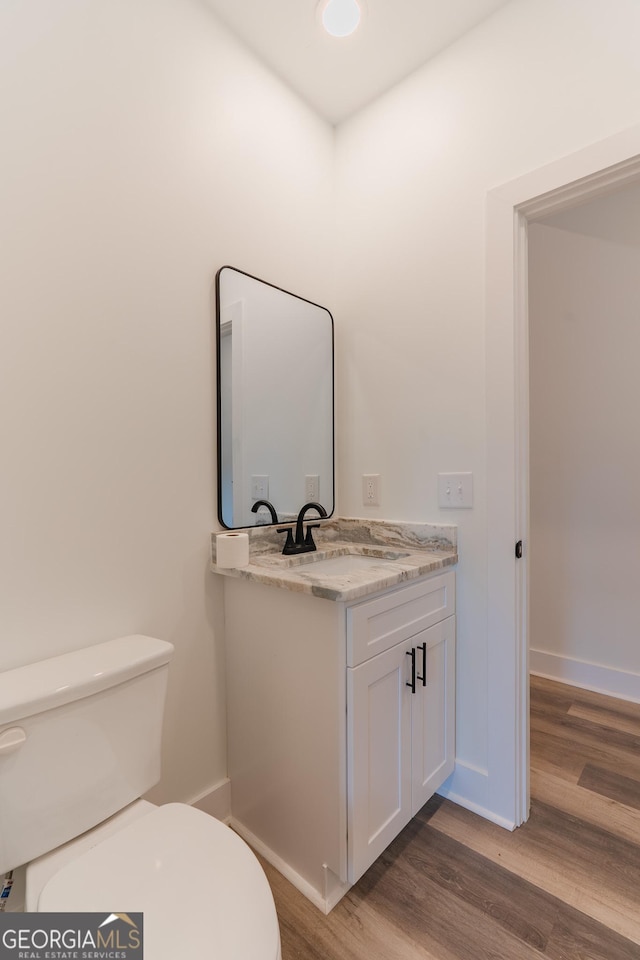 half bath with toilet, vanity, baseboards, and wood finished floors