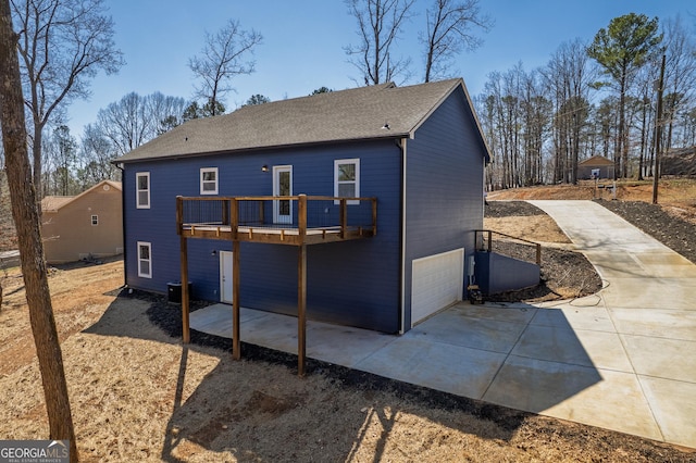 back of property with an attached garage, central AC, a shingled roof, concrete driveway, and a deck