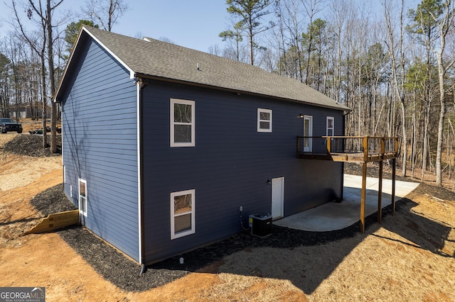 rear view of house with roof with shingles, central AC, and a deck