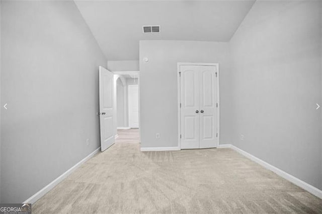 unfurnished bedroom with light carpet, a closet, and lofted ceiling