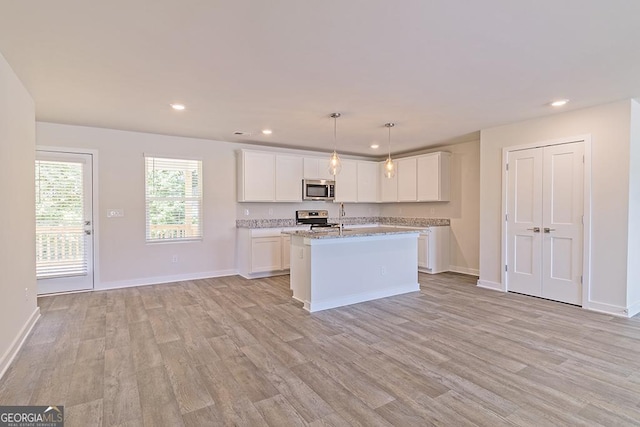 kitchen with light stone countertops, stainless steel appliances, decorative light fixtures, a kitchen island with sink, and white cabinets