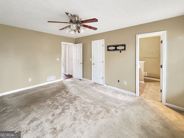 unfurnished bedroom with carpet, ceiling fan, ensuite bathroom, and a textured ceiling