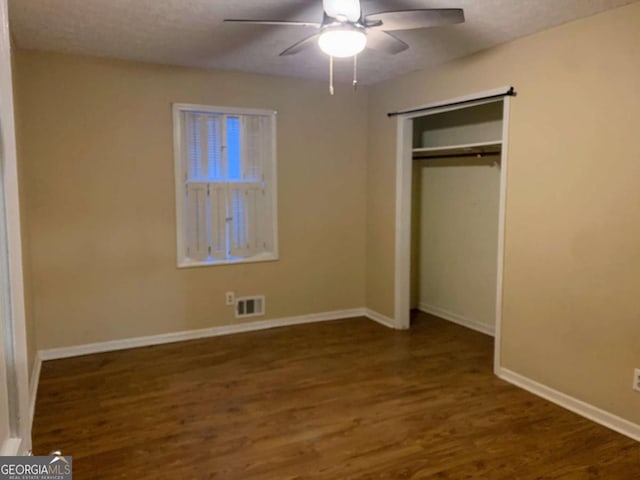 unfurnished bedroom featuring dark wood-type flooring, a textured ceiling, ceiling fan, and a closet