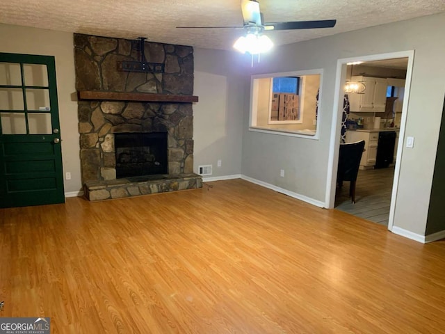 unfurnished living room with ceiling fan, a stone fireplace, a textured ceiling, and light wood-type flooring