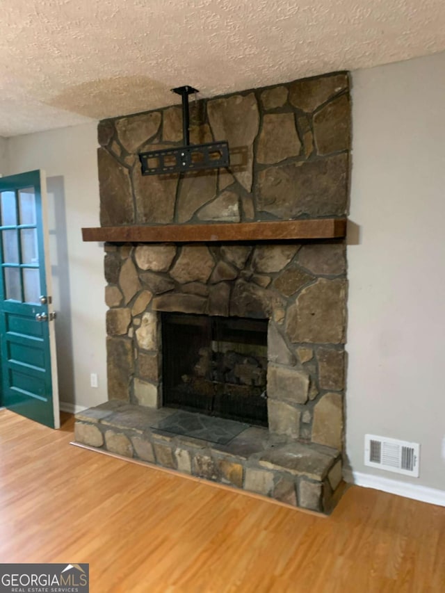 interior details featuring a stone fireplace, hardwood / wood-style floors, and a textured ceiling