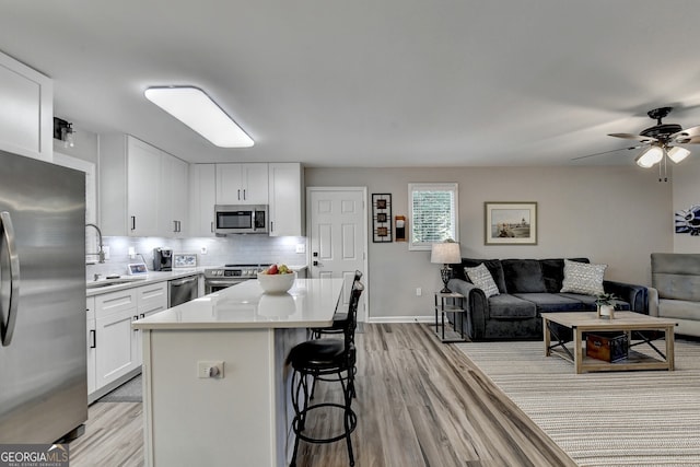 kitchen featuring a center island, light hardwood / wood-style flooring, backsplash, white cabinets, and appliances with stainless steel finishes