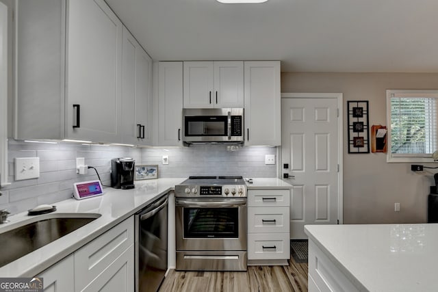 kitchen with sink, appliances with stainless steel finishes, decorative backsplash, white cabinets, and light wood-type flooring