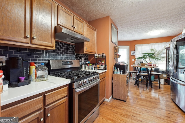 kitchen with appliances with stainless steel finishes, a textured ceiling, tasteful backsplash, and light hardwood / wood-style floors