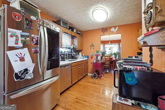 kitchen with light wood-type flooring, a textured ceiling, stainless steel appliances, pendant lighting, and an inviting chandelier