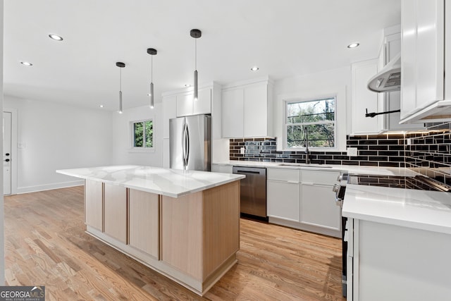 kitchen with light stone countertops, stainless steel appliances, a kitchen island, pendant lighting, and white cabinetry