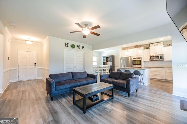 living room with ceiling fan, ornamental molding, and light hardwood / wood-style flooring