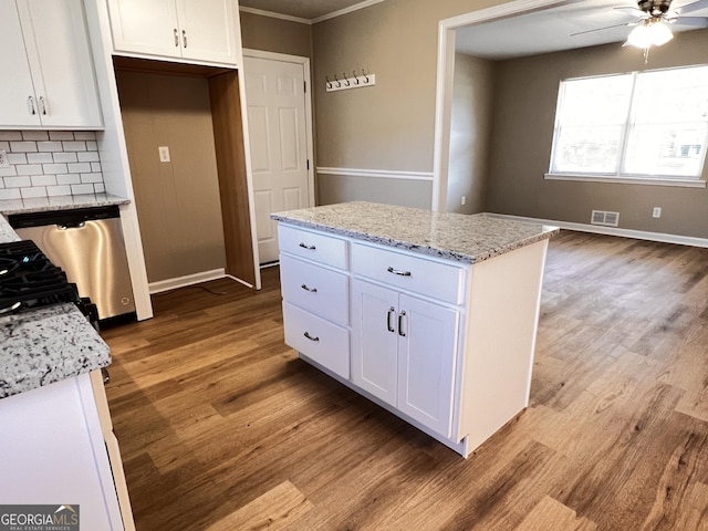 kitchen featuring light stone countertops, decorative backsplash, a kitchen island, dishwasher, and white cabinetry