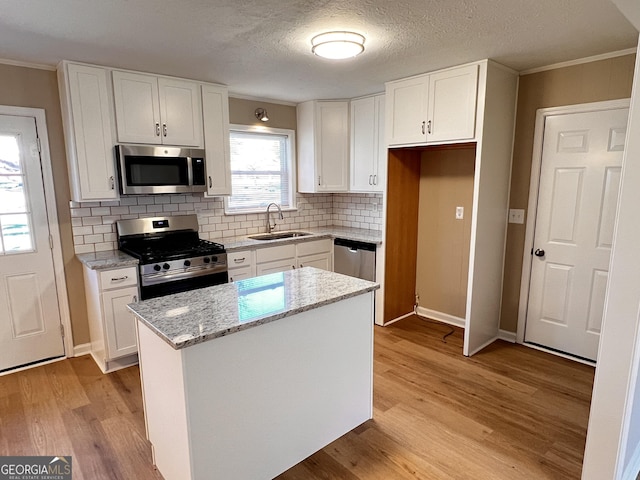 kitchen with light stone countertops, sink, a kitchen island, white cabinets, and appliances with stainless steel finishes