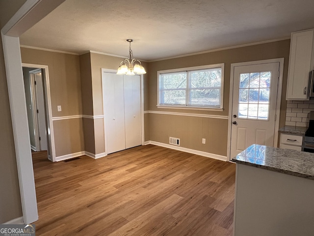 unfurnished dining area with a textured ceiling, light hardwood / wood-style floors, an inviting chandelier, and ornamental molding